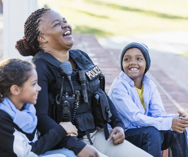 Woman police officer sitting between two kids who are smiling